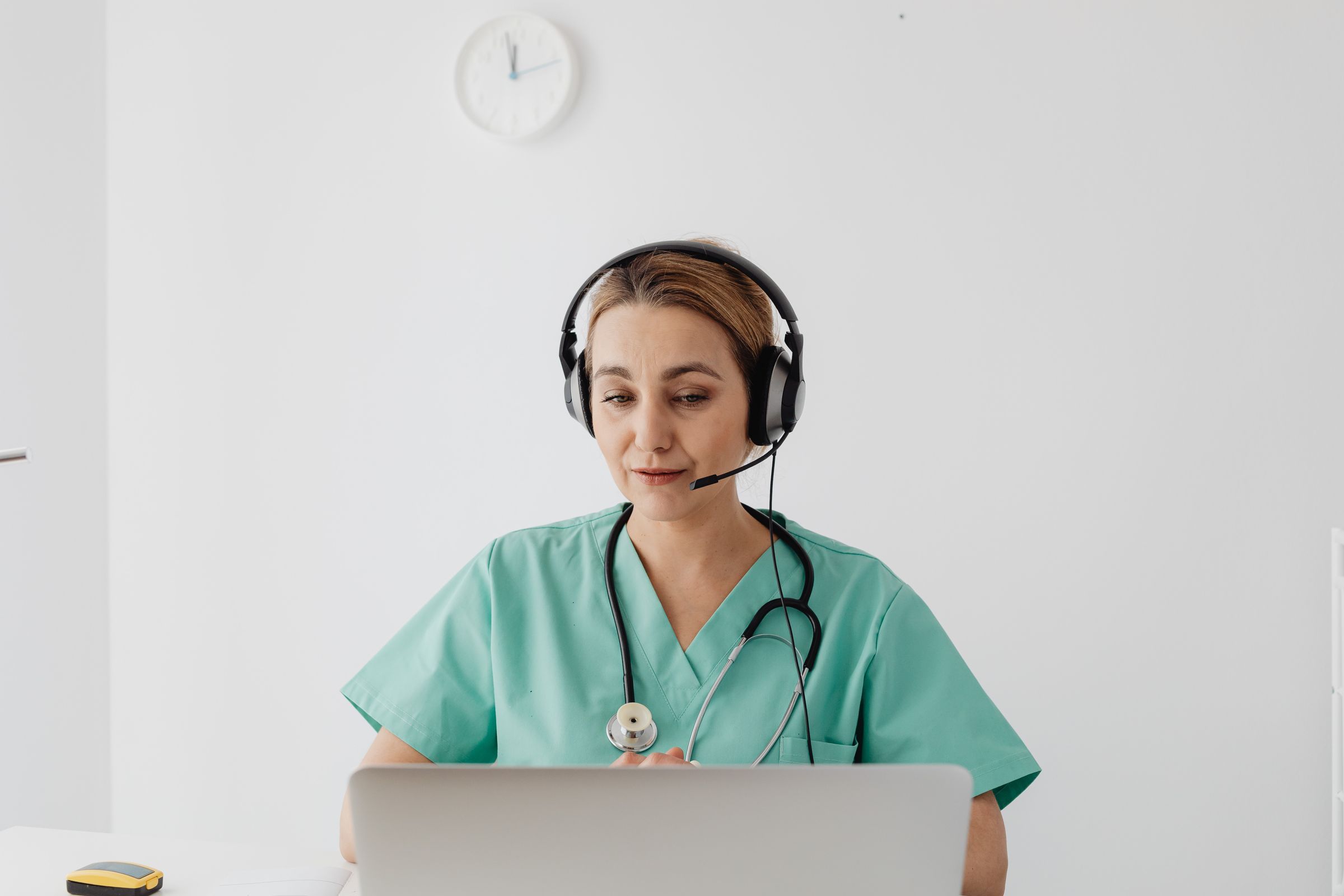 A clinician wearing a headset talks with a patient from her laptop.