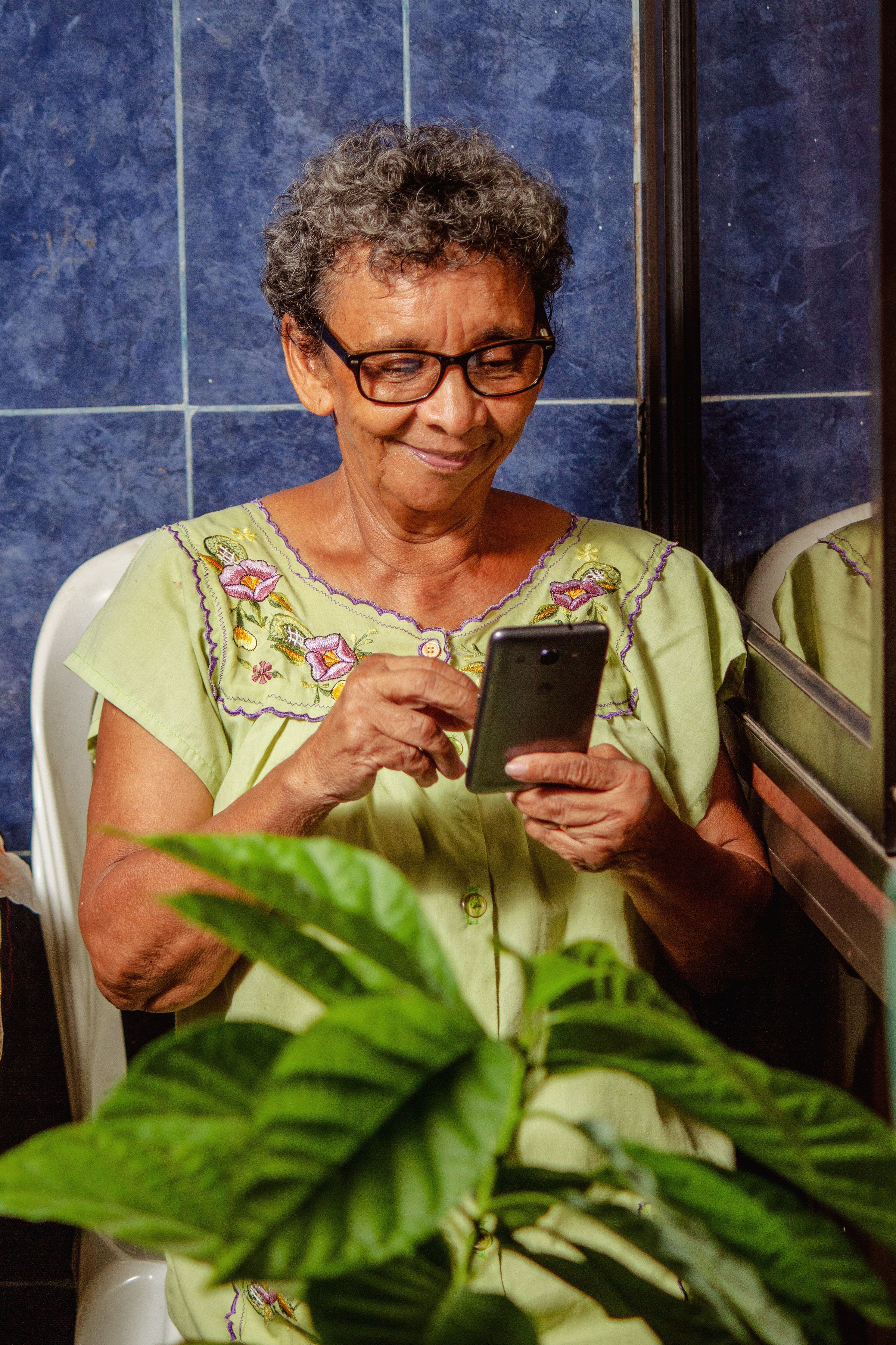 An older woman smiles as she reads a message on her phone at home.